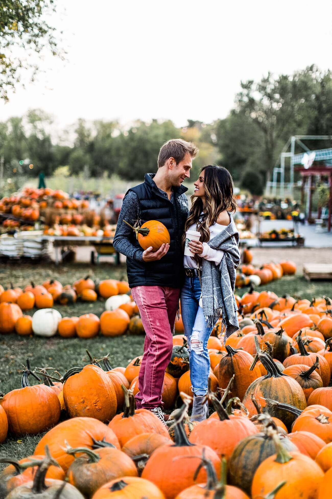 mia mia mine wearing a fall outfit at a pumpkin patch with husband