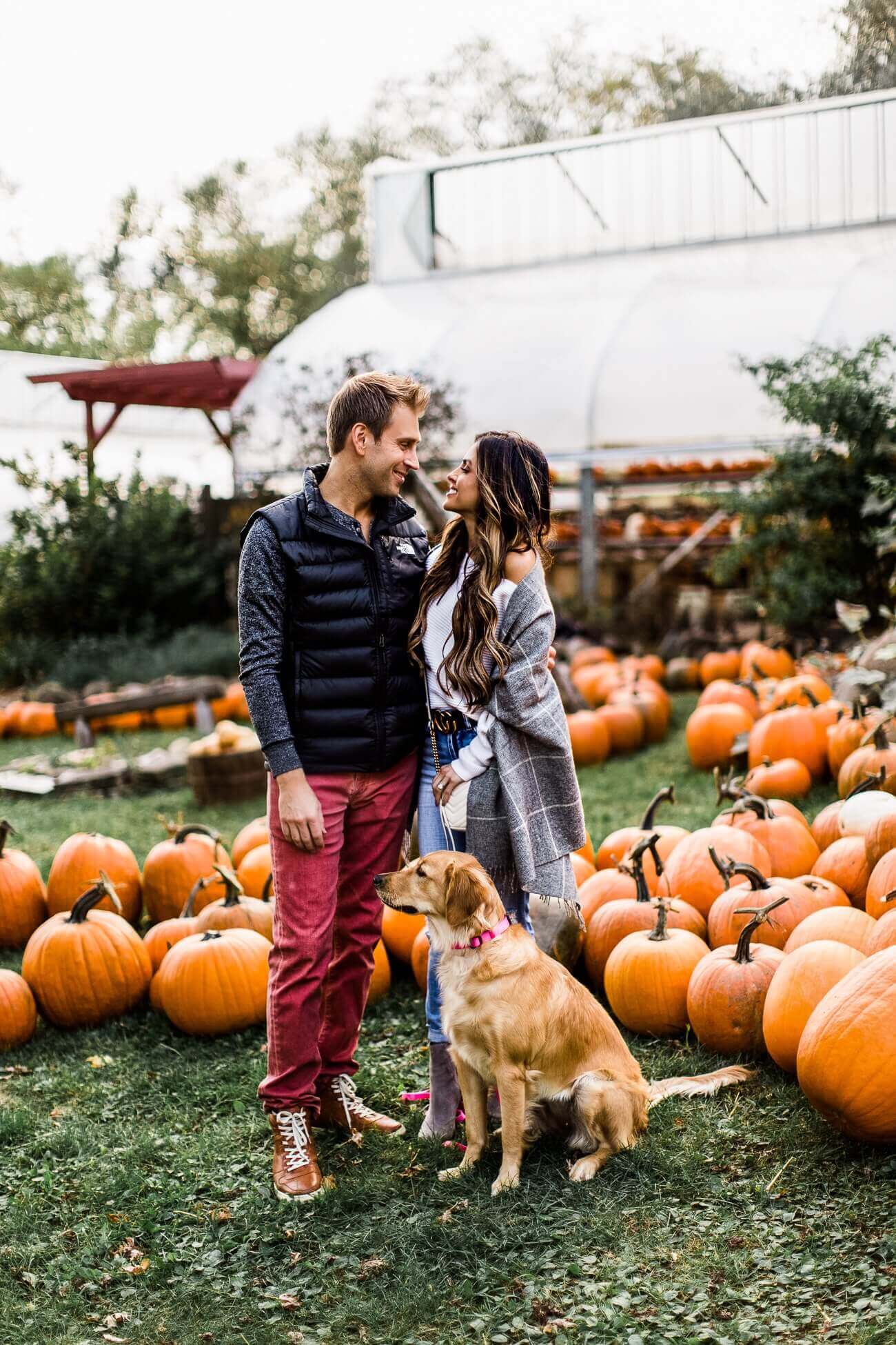 mia mia mine wearing a fall outfit at a pumpkin patch with husband