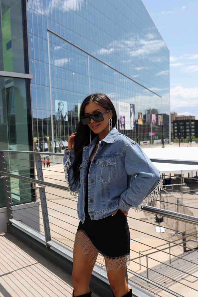 fashion blogger wearing an embellished denim jacket and embellished dress for a country concert